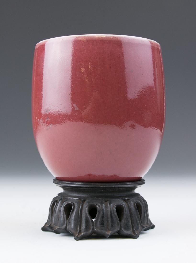 An Ox-Blood Glazed Cup: A porcelain cup, of deep sides rising from the tapered foot to a flared rim, applied overall with a lustrous ox-blood glaze thinning at the mouth in white tone, diameter 8.5 cm, height 9.5 cm
