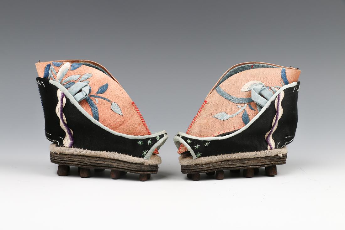 PAIR OF SILK LADIESâ€˜ SHOES, C. 1920: With a high heel and pointed toe, the orange ground embroidered in blue threads with flowers, the shoes for bound feet is comprising of two parts and set on a wooden base. 8.5cm x 10.5cm x 5cm each