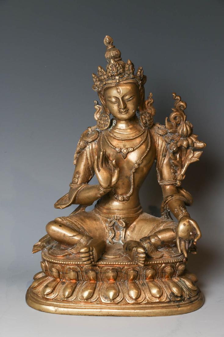 GILT BRONZE BUDDHIST FIGURE, 17TH/18TH C.: Seated in Lalitasana on a double lotus base, her hands in Vitarkamudra, clad in a dhoti secured with an elaborate belt, adorned in various jewelry and flanked by lotus blossoms at her shoulders. H:19c