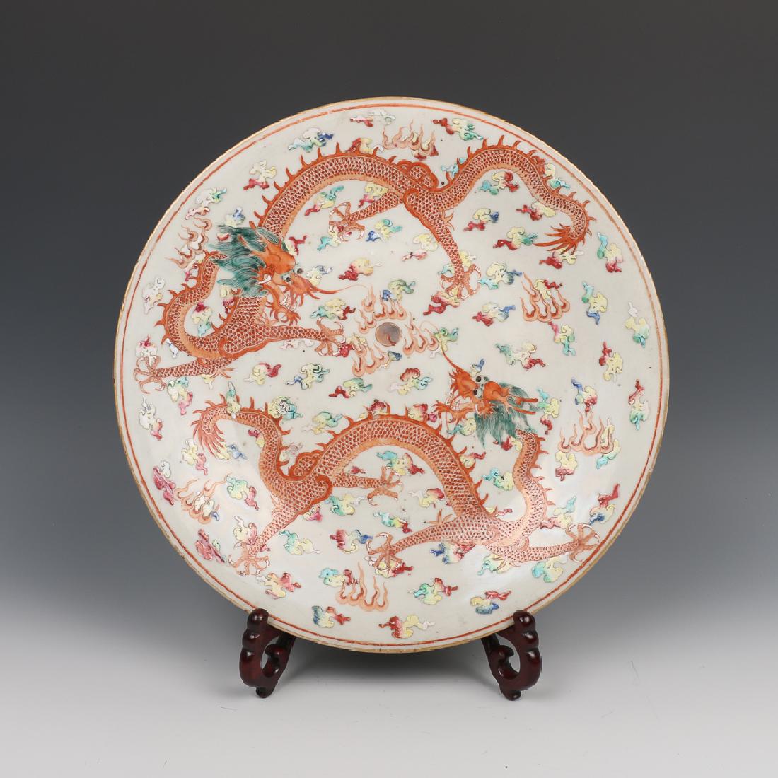 FAMILLE-ROSE DRAGON CHARGER, LATE QING: Depicting two dragons in pursuit of a flaming pearl amidst colorful scrolling clouds, the back painted with scrolling lotus blossom, the unglazed foot ring reveals the buff ware. D:30.5cm