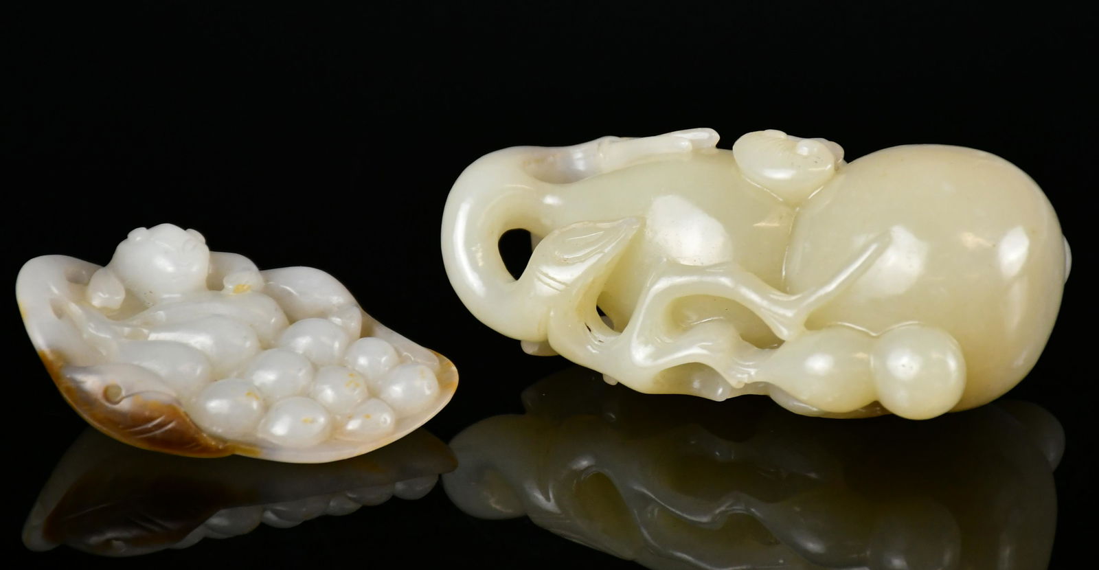 Two Celadon Jade Fruit Carvings: The first naturalistically carved issuing from a gnarled branch bearing long curling tendrils and smaller double-gourds. The second carved as a bunch of grapes born on a leafy stem, the stone of pale