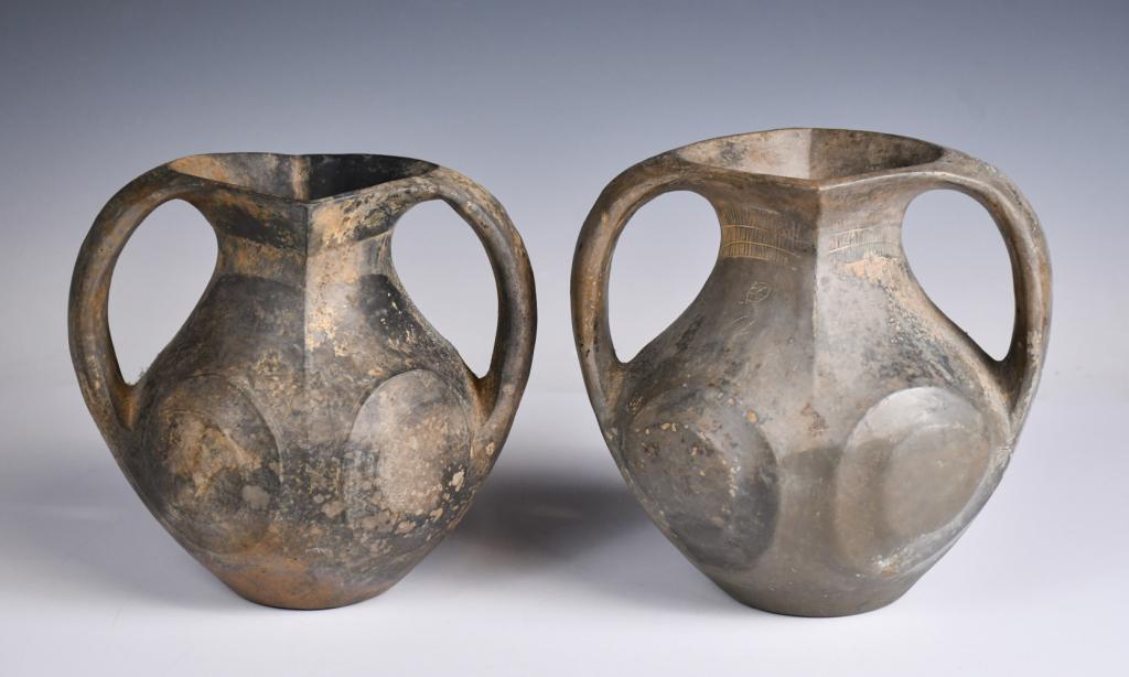 Pair of Black Glazed Amphoras, Han Dynasty: Each globular body connects up to a diamond mouth, flanked to the sides with a pair of thick strap handles, incised with mythical patterns to the body. H: 16.3cm & 17.5cm Provenance: H.H. Pao's previo