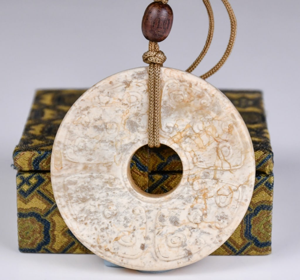 An Archaistic Chicken-Bone Jade Bi Disc w/Box: Of typical Bi disc form, carved with motifs on both side, the stone of greyish white color. D:5.5cm Provenance: Vancouver Hong Kong Immigration 高古風格雞骨白