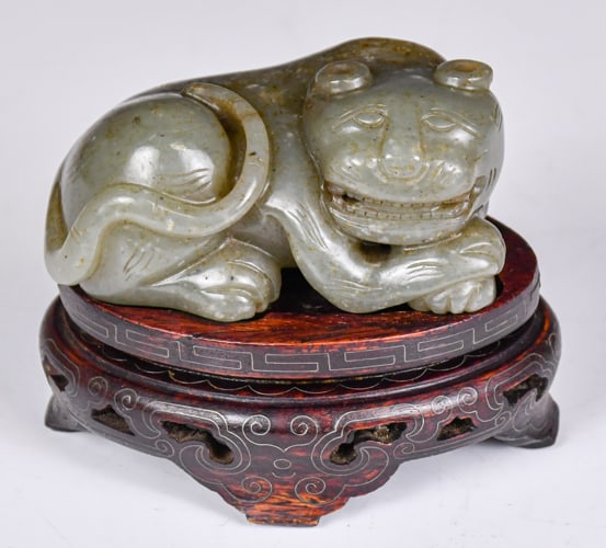 A Celadon Jade Carved Beast W/ Std Republican: A beast carved from a gray celadon stone with russet and white inclusions, in a prone position. With the beast's head turns to it's right. L: 8.6 x H: 4 x W: 5cm 民國 青玉Ƃ