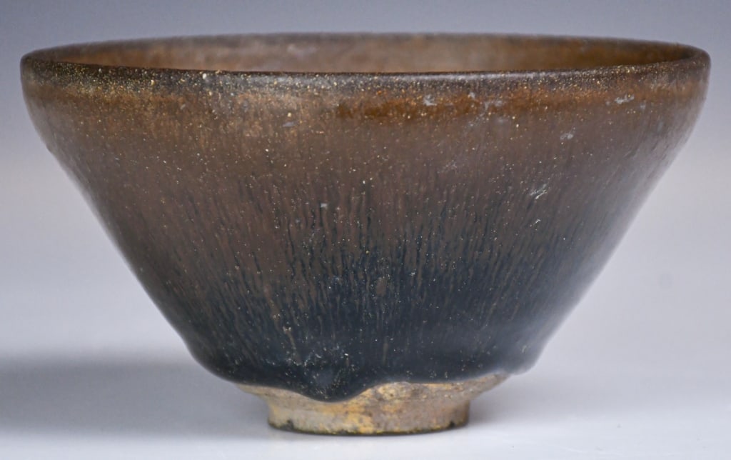 A Song-Style Jian Kiln Tea Cup: The bowl features a narrow rim, a slightly tapering belly, and a low, ring-shaped foot. It is glazed entirely in black, with dense golden stripes resembling rabbit hair and a multicolored sheen. D: 13