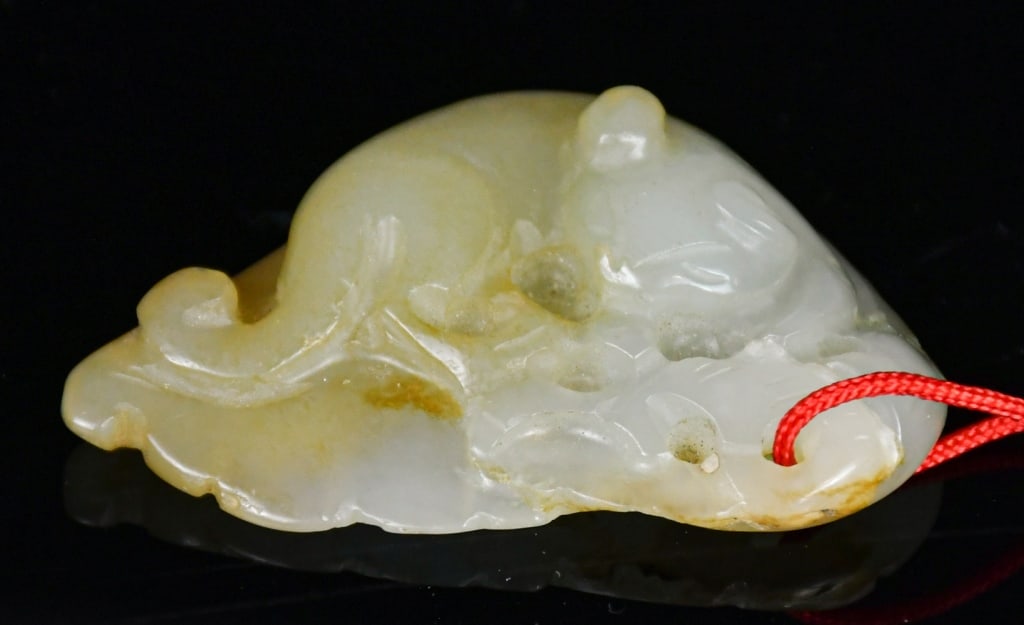 A Celadon Jade Badger Qing: A jade carved badger on a leaf, the stone overall in pale celadon color tone, L:4.7cm 清 青白玉雕一葉獾吊飾