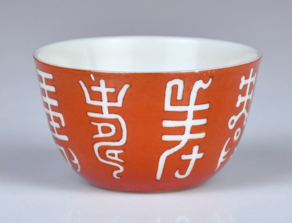 An Iron Red Cup Republican w/Mk: Decorated to the exterior with white Chinese characters arranged in bands, the gently rounded sides rising from a short recessed foot; with a mark at the bottom. H:3.5cm, D:6.2cm 民國 
