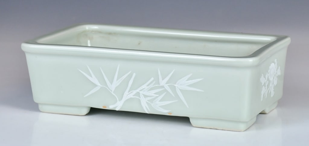 A Celadon Glazed Square Narcissus Pot Republican: Of rectangular form, supported on four short feet, the sides applied in relief with blossoming flowers and bamboo, covered overall in celadon glaze. 25x15x7.5cm 民國 綠釉ฒ