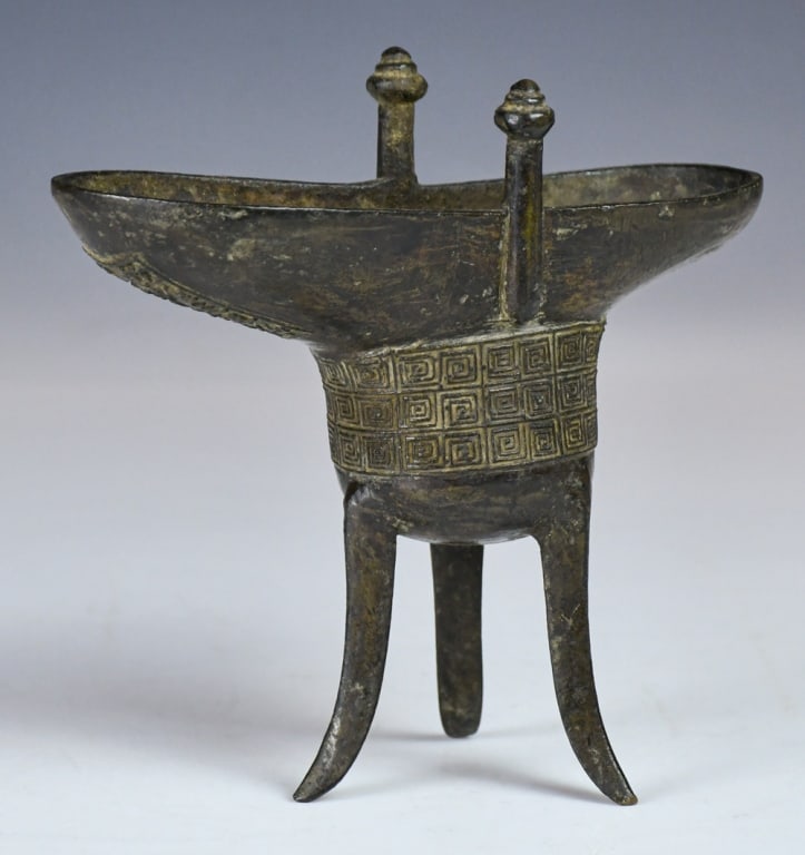 A Bronze Jue-Form Libation Vessel Ming Dynasty: With a U-shaped body raised on three splayed legs, the exterior incised with geometric motifs and a Chinese-character mark. H: 15.8cm 明 青銅三足爵杯