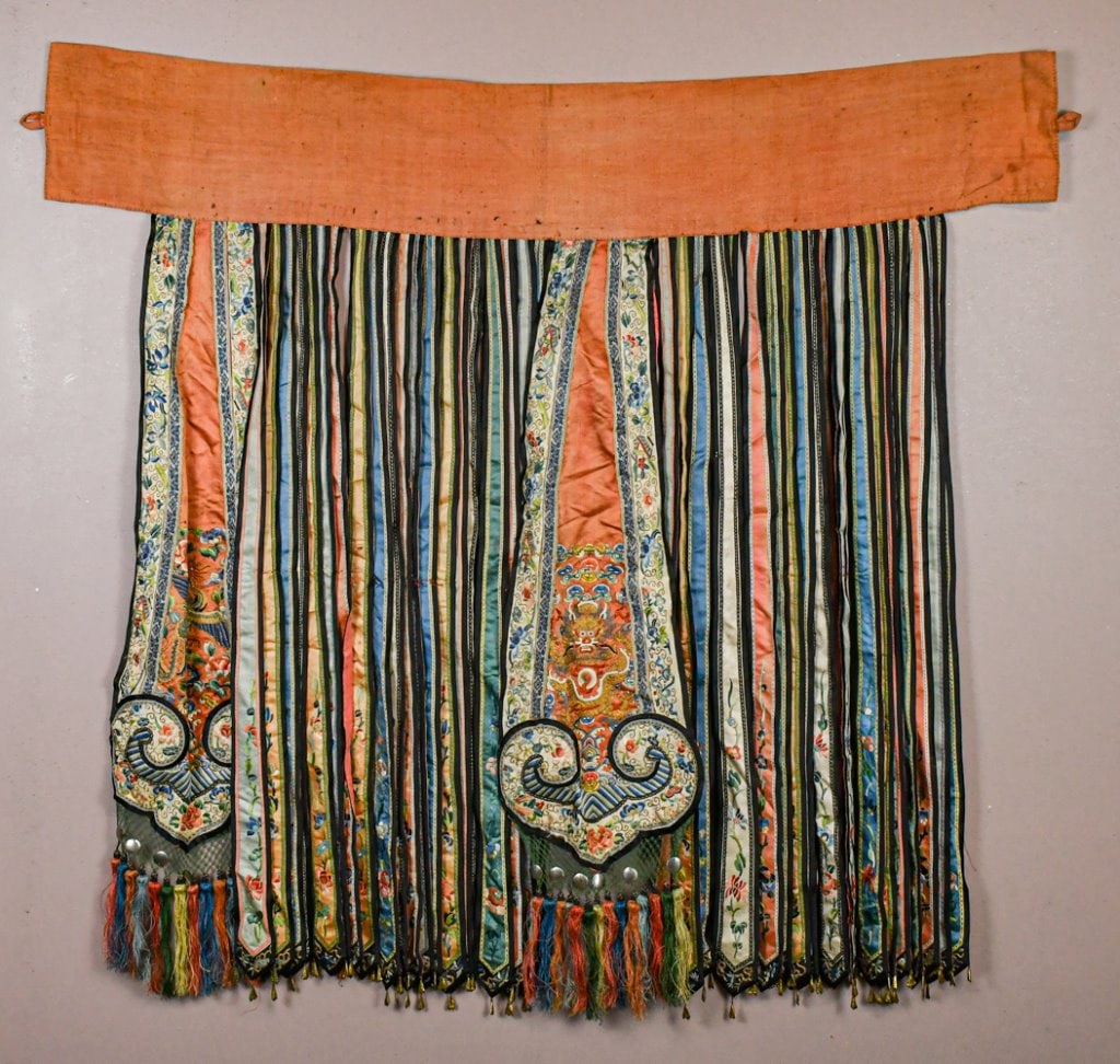 A Chinese Embroidered Overskirt Qing: Of phoenix-tail construction, suspending numerous vertical silk panels, including two ruyi-shaped panels embroidered with dragons and scrolling motifs, the ends finished with silk tassels, 