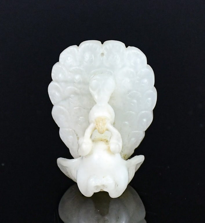 A White Jade Peacock Carving Republican: Carved as a peacock, the plumage finely detailed, the sweeping tail feathers incised with patterns, the bird grasping a ruyi spray in its beak. 3.5 x 2.7cm 民國