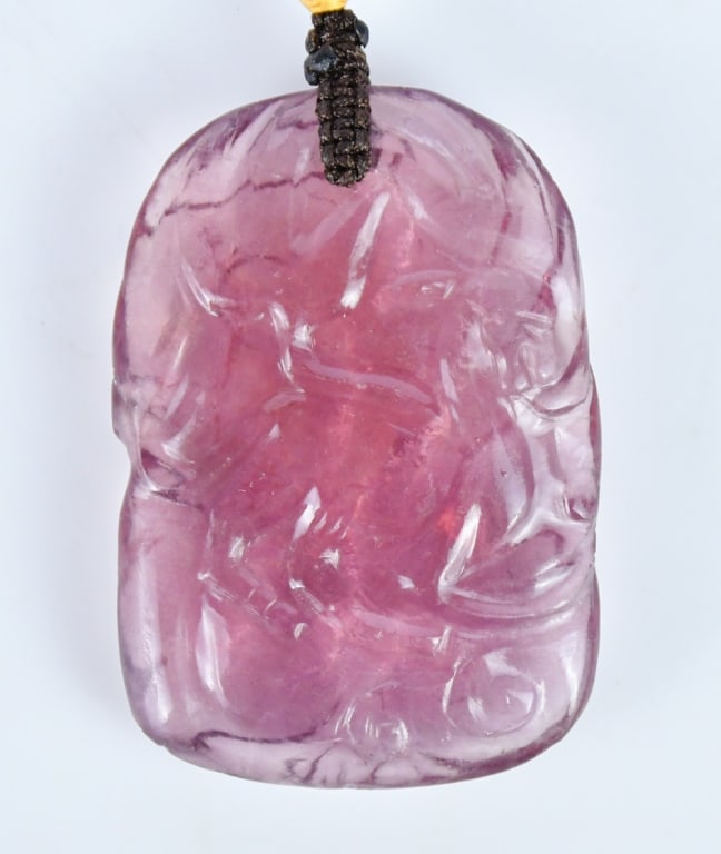 A Carved Tourmaline Pendant Republican: Of rectangular form, carved in relief with a mythical beast amid scrolling motifs, the semi-translucent stone of purplish tone. 5.8x3.9cm 民國 碧璽掛件 