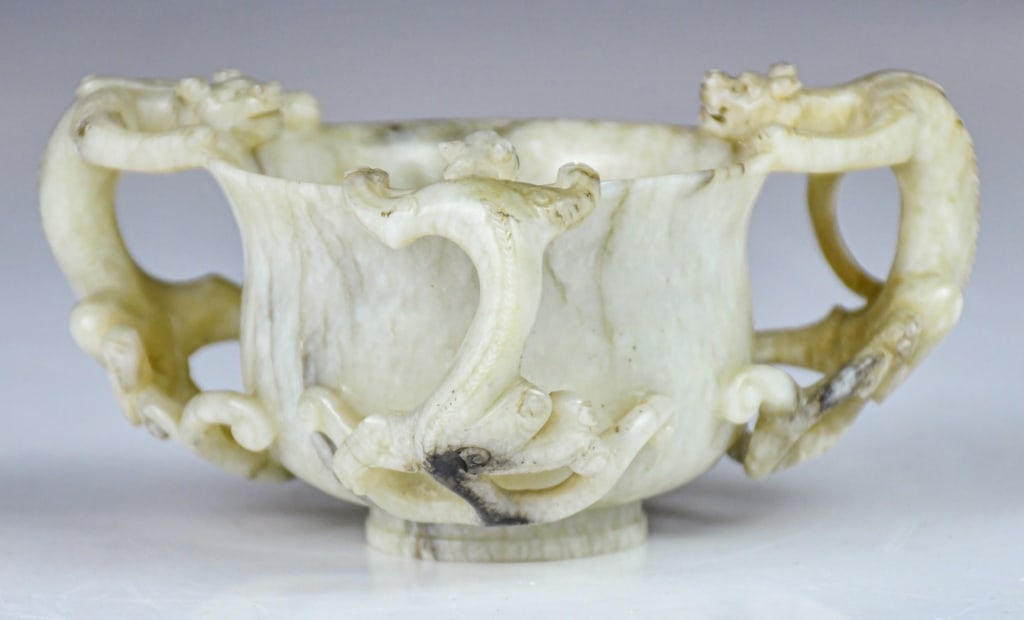 a Grayish-White Jade Cup w/Chilong Handles, Ming: Carved around the sides with three chilong clambering up from the bottom to the slightly everted rim. The semi-translucent stone has some dark brown speckling and some opaque buff mottling.