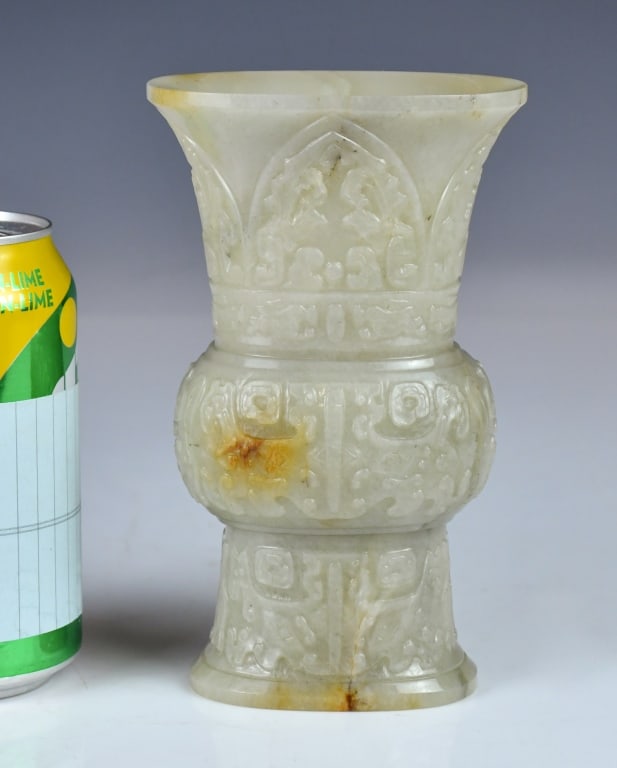 A Jade Carved Gu-form Vessel Qianlong Period: A jade vessel modeled after archaic bronze gu ritual wine vessels, carved around the exterior with archaic-style patterns, including what appear to be taotie beast-face motifs. Four-character 