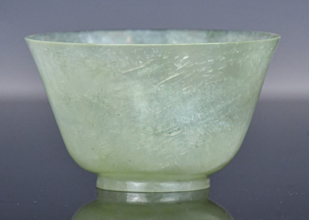 A Jadeite Carved Bowl Republican: The deep round side rising from the short feet to the flared rim, the stone overall in translucent celadon color. D:8.5cm, H:5cm 民國 翡翠茶杯