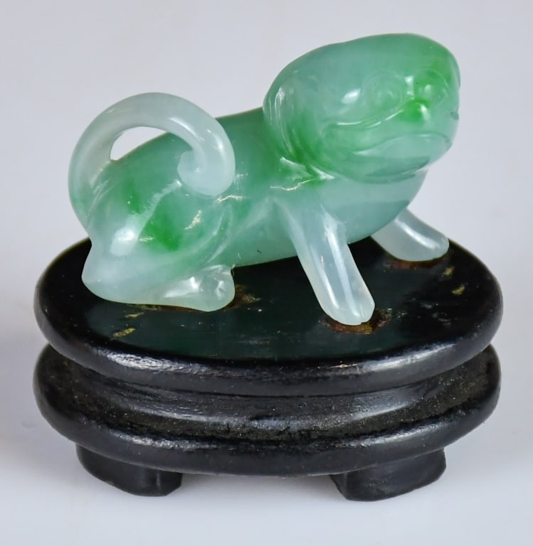 A Jadeite Carved Dog w/Std: A jade carving of a dog in a squatting position, in celadon and green tone, comes with a wood stand. 3.9x1.5cm 翡翠犬擺件 連座 Click here for