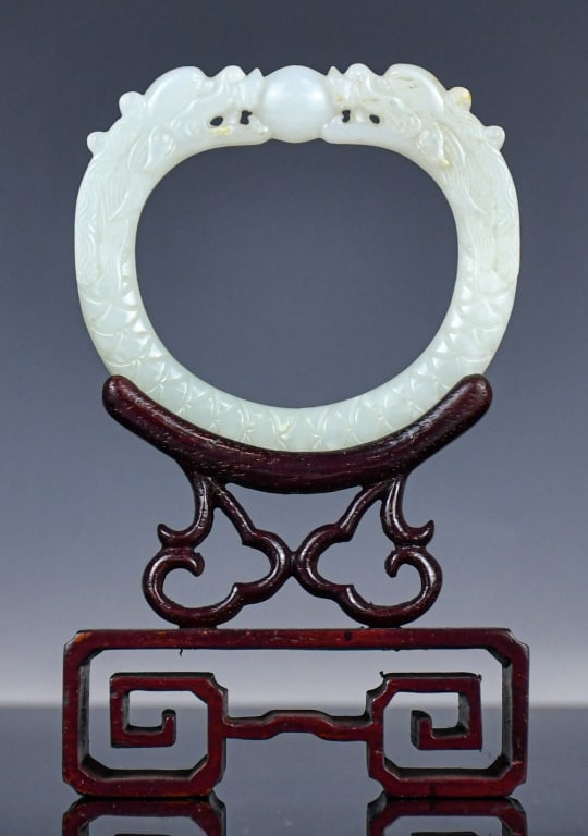 A Carved Jade Dragon Ring Ornament Republican: Carved in relief with two dragons, their sinuous bodies forming a continuous hoop and centred on a raised bead; comes with a stand.outer: 8x8.8cm, inner: 5.4x6.4cm 民國