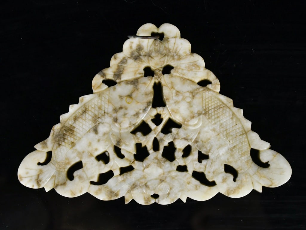 A Reticulated Jade Pendant Qing: Of triangular outline, finely carved in openwork relief with two fish set amidst scrolling leafy foliage, the stone of mottled russet tones. 13.3x8.8cm 清