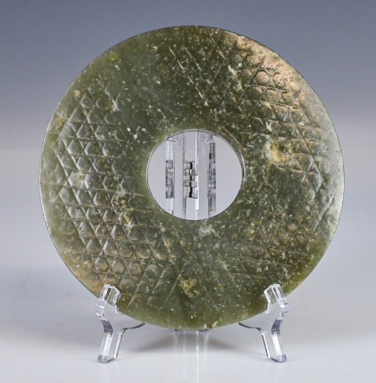 An Archaistic Large Jade Bi Disc: Of circular form with a central aperture, carved on both sides with geometric lattice patterns, one face flat and the other slightly domed, the stone of dark celadon tone. D: 15.8cm 