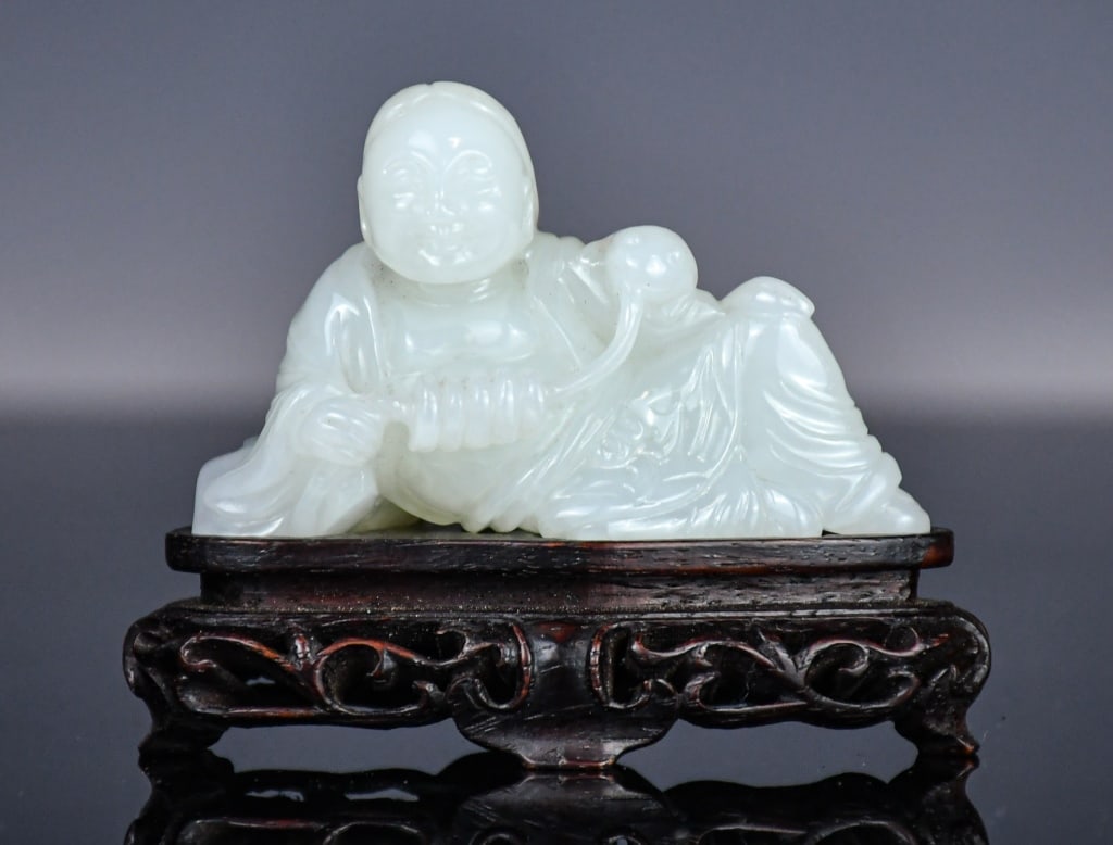 A White Jade Carved Figure w/Stand Republican: Depicting a reclining figure propped on one elbow, a frog perched on his upper arm, its tongue extended; comes with a wood stand. 7.1x4.7cm 民國