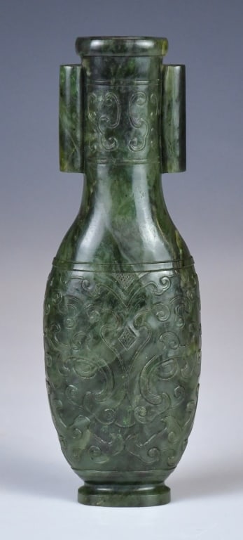 A Small Spinach Jade Vase Republican: Carved from dark green jade, with a cylindrical mouth, short neck, sloping shoulders, a flattened body, and a slightly flared foot. The neck is flanked by a pair of raised vertical flanges. The 