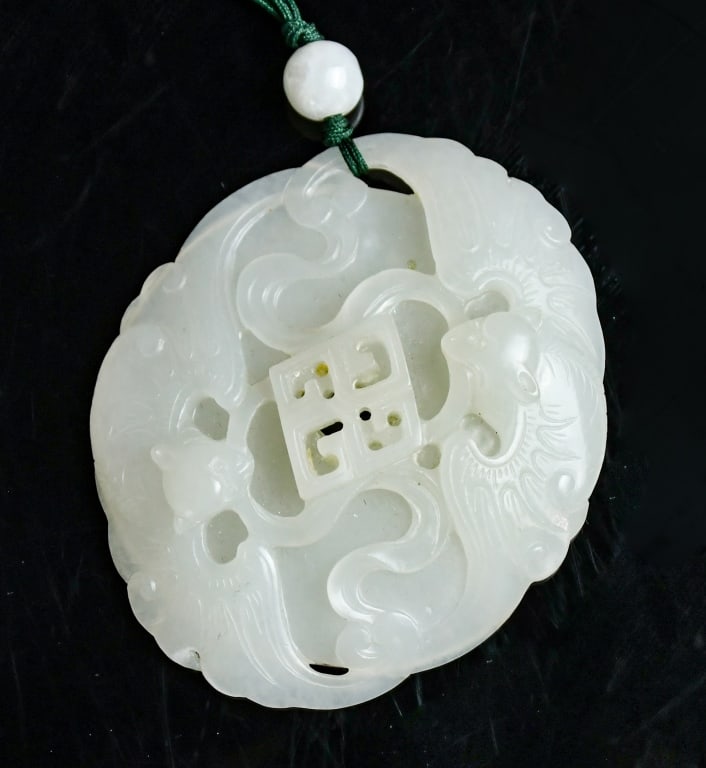 A White Jade Carved Bats Plaque Qing: Carved with two bats surrounding a central square aperture, with scrolling motifs along the border, the reverse incised with two characters, the stone of pale celadon-white tone. 6.5x5.5cm 