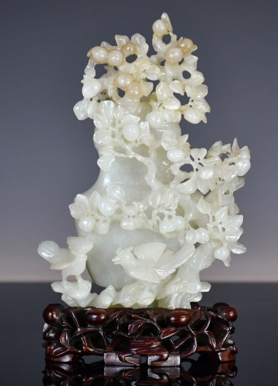 A Jade Stone Carved Vase w/Cover & Std 1950-70s: A jade carved covered vase, of baluster form, decorated with peach tree and two birds, the stone overall in slightly translucent white tone, vase with cover H:17cm, comes with a wood stand. 