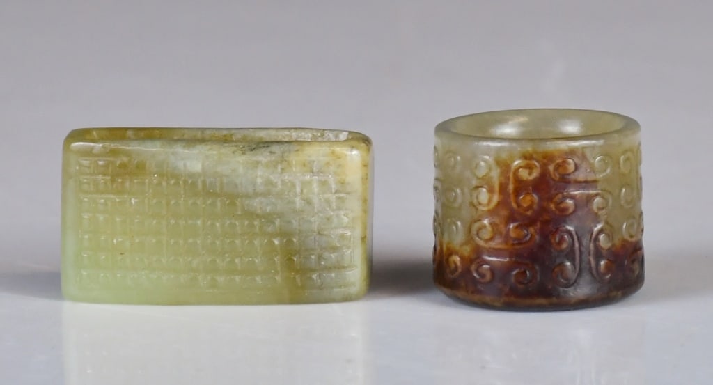 An Archaistic Jade Sword Fitting & A Thumb Ring: Comprising a sword fitting:4.5x2.3cm, and a jade thumb ring D:3cm, H:2.5cm 高古風格 玉劍飾及玉扳指 Click here for natural
