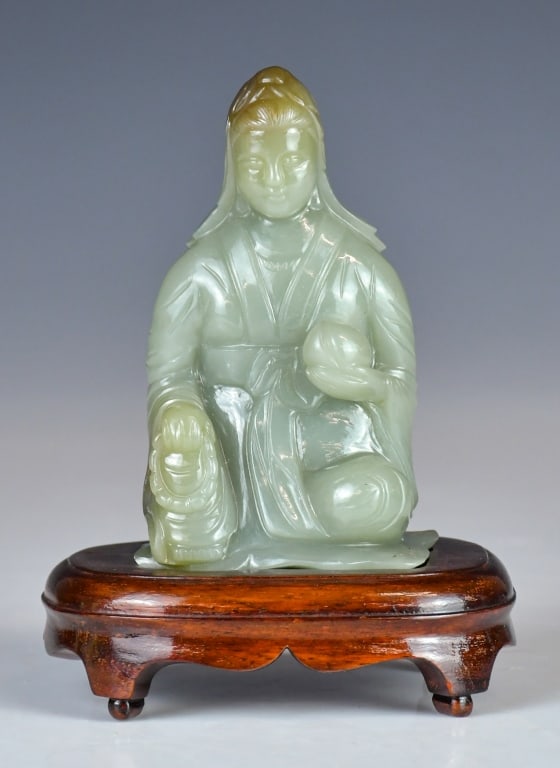 A Celadon Jade Carved Figurine w/Std 1950-70s: Carved as a figure sitting, holding a string of beads in one hand and a peach in the other, overall in celadon tone with russet shades, H:11cm, comes with a stand. 建國期 青