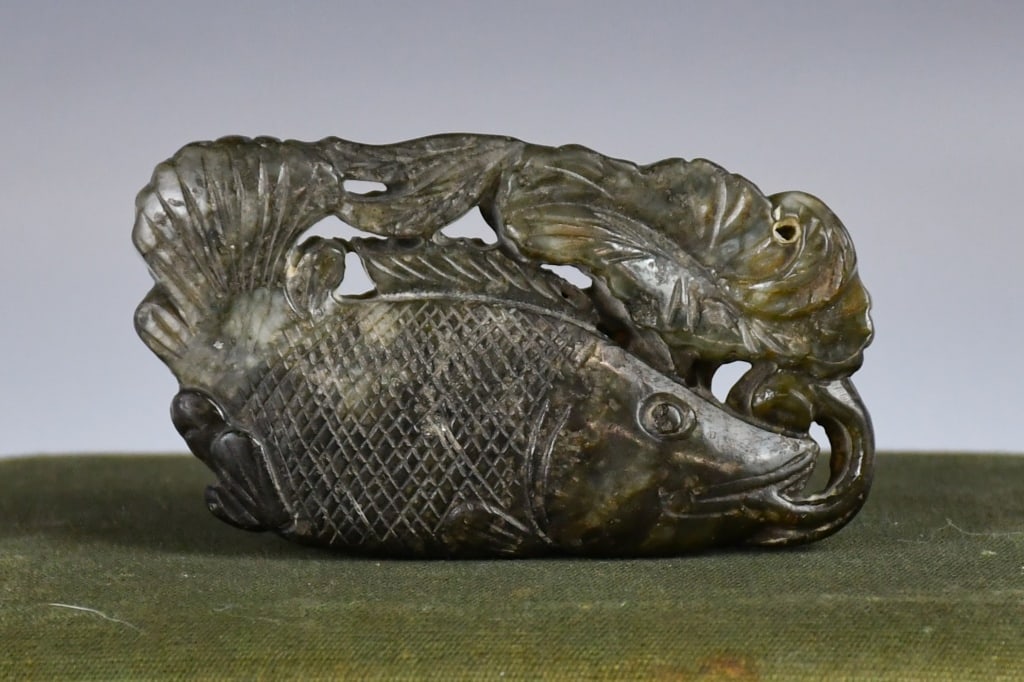 An Archaitstic Jade Carved Fish Ornament w/Box: Carved as a fish grasping a lotus leaf, the body detailed with cross-hatched scales, the stone of dark celadon tone. 6.5 x 3.9cm 高古風格玉雕魚形把