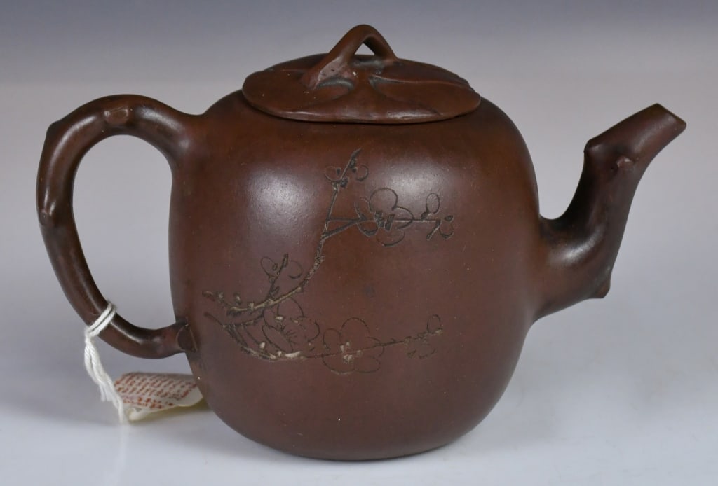 A Carved Papaya Zisha Teapot 19thC: The body is rounded and full, mimicking the shape of the fruit. The spout and handle are naturalistically modeled as gnarled tree branches with knot details. D:20cm, H:11.5cm Provenance: H.H.