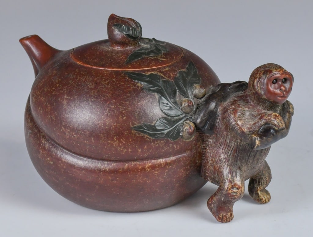 A Monkey & Peach Zisha Teapot: Of compressed globular form, the body artfully modeled in the shape of a longevity peach, and applied low-relief peach leaves and branches extending from the handle. The handle is sculpted as a