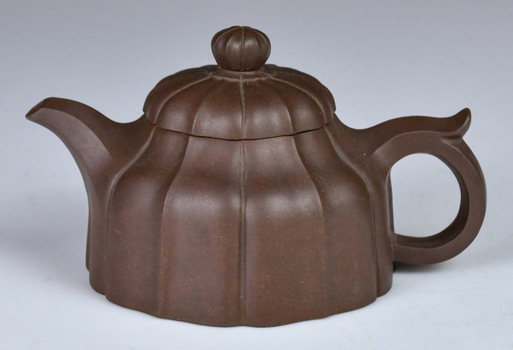 A Ribbed Chrysanthemum Zisha Teapot: The body is skillfully divided into multiple vertical "petals" or ribs that radiate from the center. The lid continues this segmented pattern, surmounted by a matching flower-bud knot. Maker's 