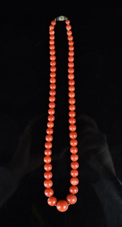 A Graduated Red Coral Bead Necklace: Composed of a single strand of 58 round coral beads, graduating in size from the smaller beads near the clasp to a prominent central bead. The coral displays an exceptionally vibrant, uniform orange-r