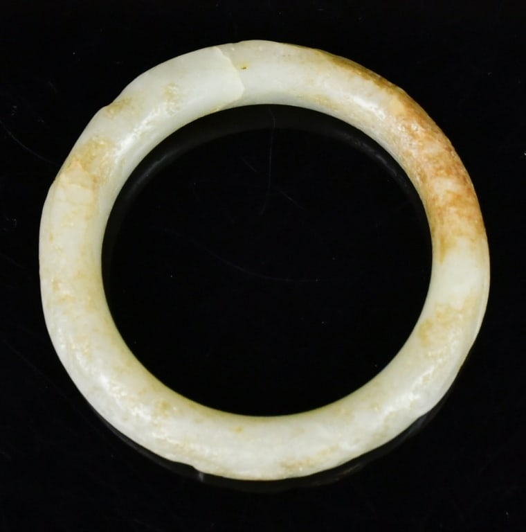 An Archaistic Jade Carved Bangle: A round shape jade carved bangle with carving of dragon-like patterns, the stone overall in pale celadon color with caramel inclusion. 59(inner D)x12x10.6mm. 高古風格青&#
