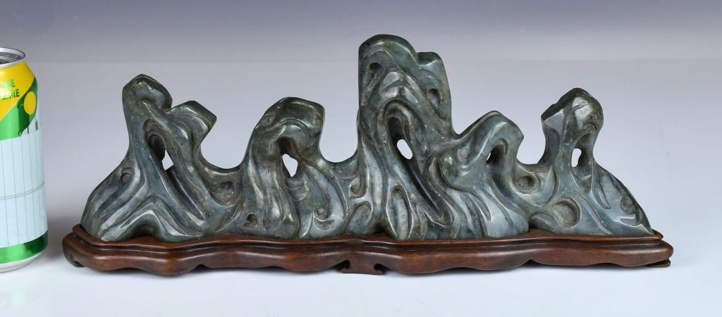 A Jade Carved Rockwork Ornament w/Std Republican: The jade carving of rockwork form, carved with pierced and curling contours, of dark celadon tone, comes with a wooden stand. 34x11.5cm 民國 玉石雕山子擺