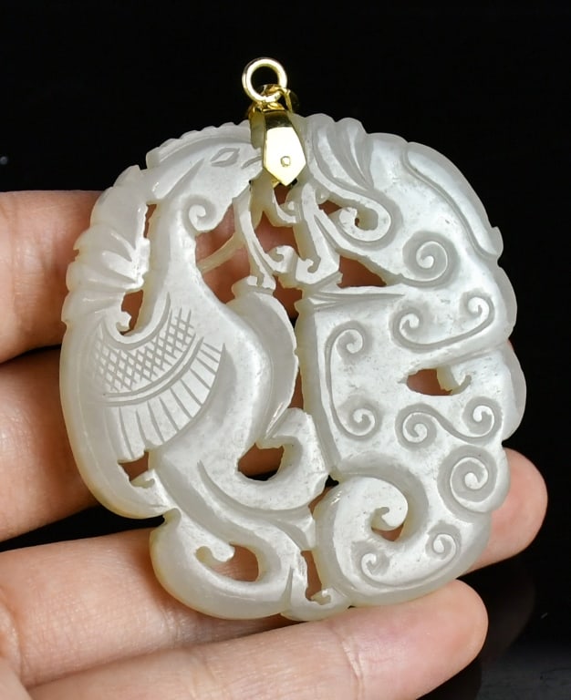 A Reticulated Jade Pendant w/14K Gold Bail Qing: Of flattened circular form, carved in openwork to depict chilong dragon arching its body opposite a slender, long-necked phoenix. The stone is of an even, translucent pale greenish-white tone. The top