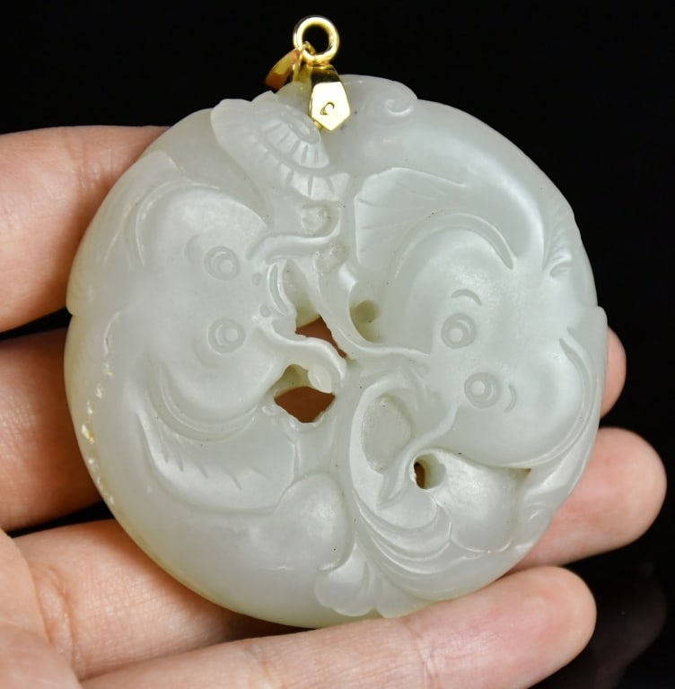 A White Jade Catfish Pendant w/14K Gold Bail Qing: A white jade round pendant featuring double-catfish and Lingzhi patterns, the top pierced with a small aperture fitted with a 14K gold bail. D:5.3cm 清 14K金白玉雙魚
