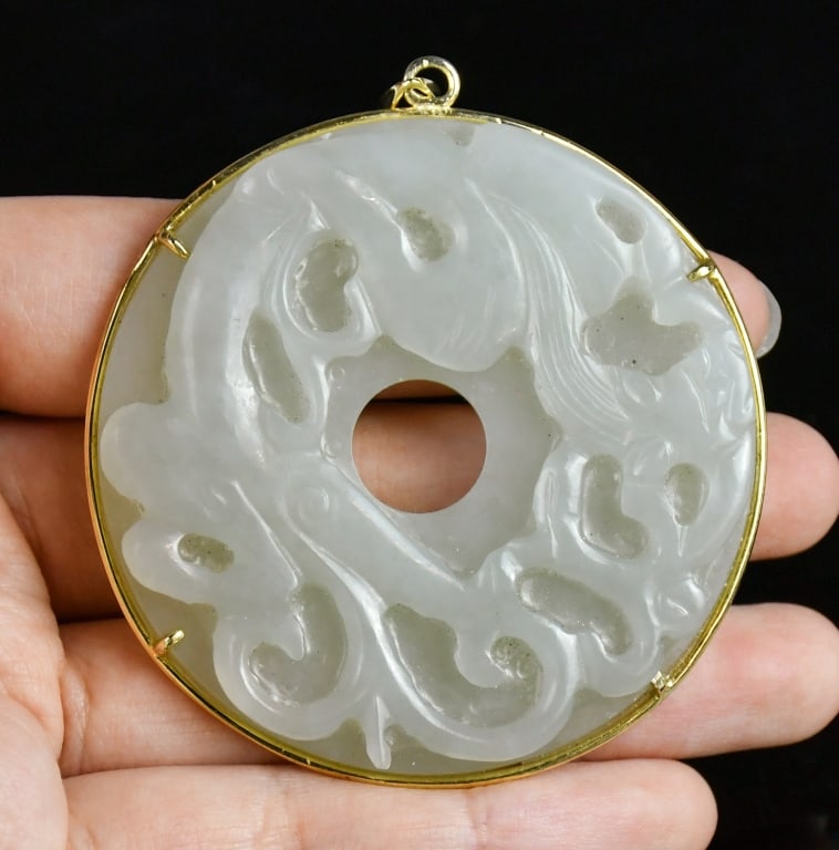 A White Jade Bi Disc Pendant w/14K Gold Bail Qing: A white jade Bi disc pendant featuring a chilong dragon carving in a gold setting, and the opposite side carved with geometrical patterns. D:5.5cm 清 14K金白玉龍紋&