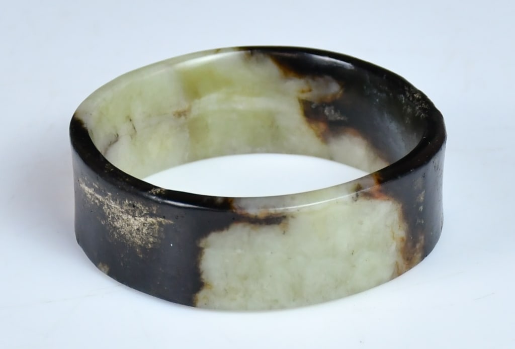 An Archaistic Jade Carved Bangle: A round shape flat jade carved bangle with flower and Lingzhi patterns, the stone overall in celadon color with dark brown inclusion. 58(inner D)x22x5.4mm. 高古風格青