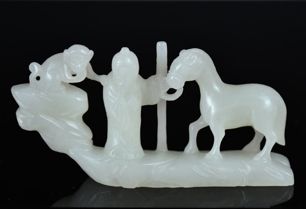 A White Jade Carved Ornament 20thC: The translucent stone of an even pale celadon-white tone with minor opaque inclusions, deftly carved in the round and pierced as a continuous openwork rocky landscape tableau depicting a scholar with 