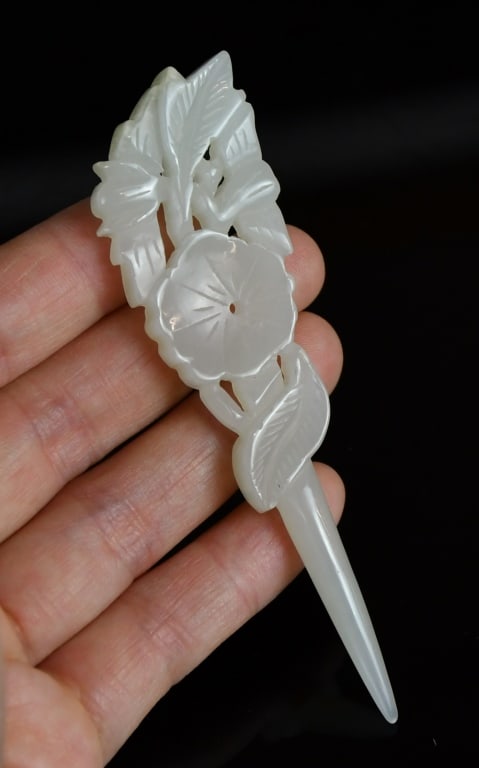 A White Jade Carved Hairpin Republican: The hairpin is carved and worked in openwork at the terminal to depict a blooming hibiscus blossom enclosed by overlapping, serrated pointed leaves and scrolling tendrils, all springing from a slender