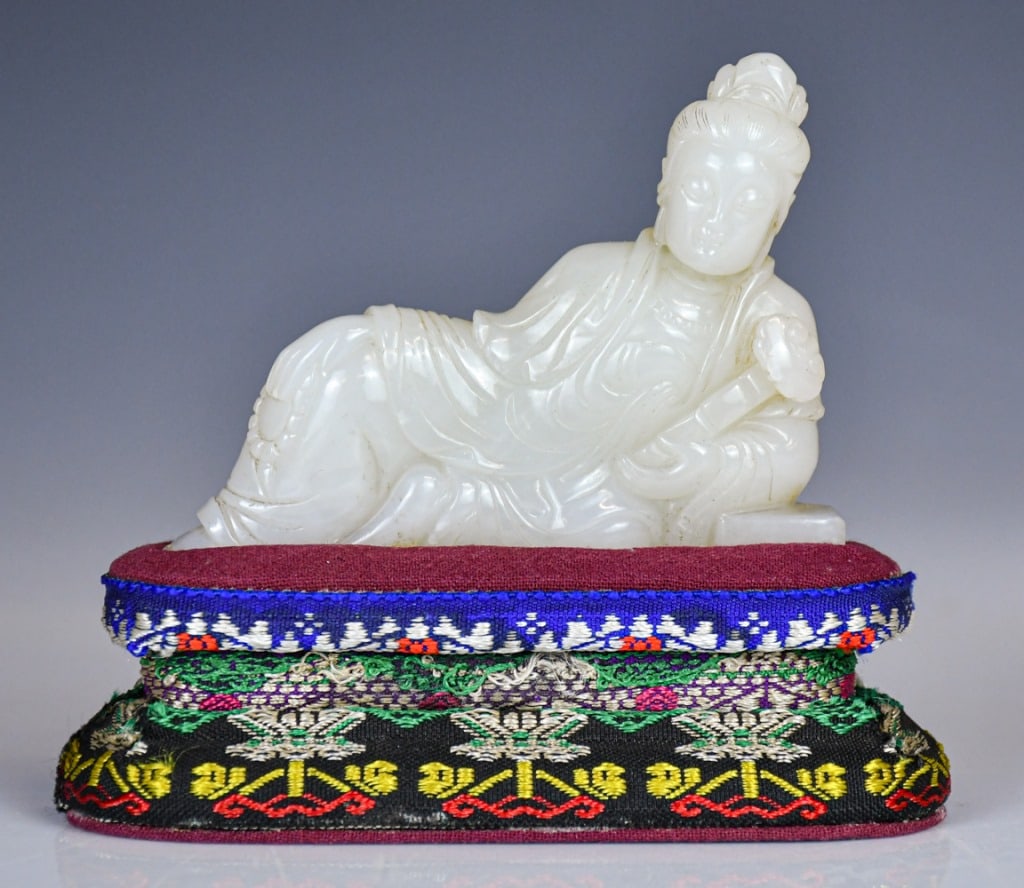 A White Jade Carved Guanyin w/Std Republican: The figure is draped in voluminous, flowing robes that fall in rhythmic, deeply undercut folds around the body, with Ruyi on hand, the stone is of an exceptionally even, translucent milky-white tone. 