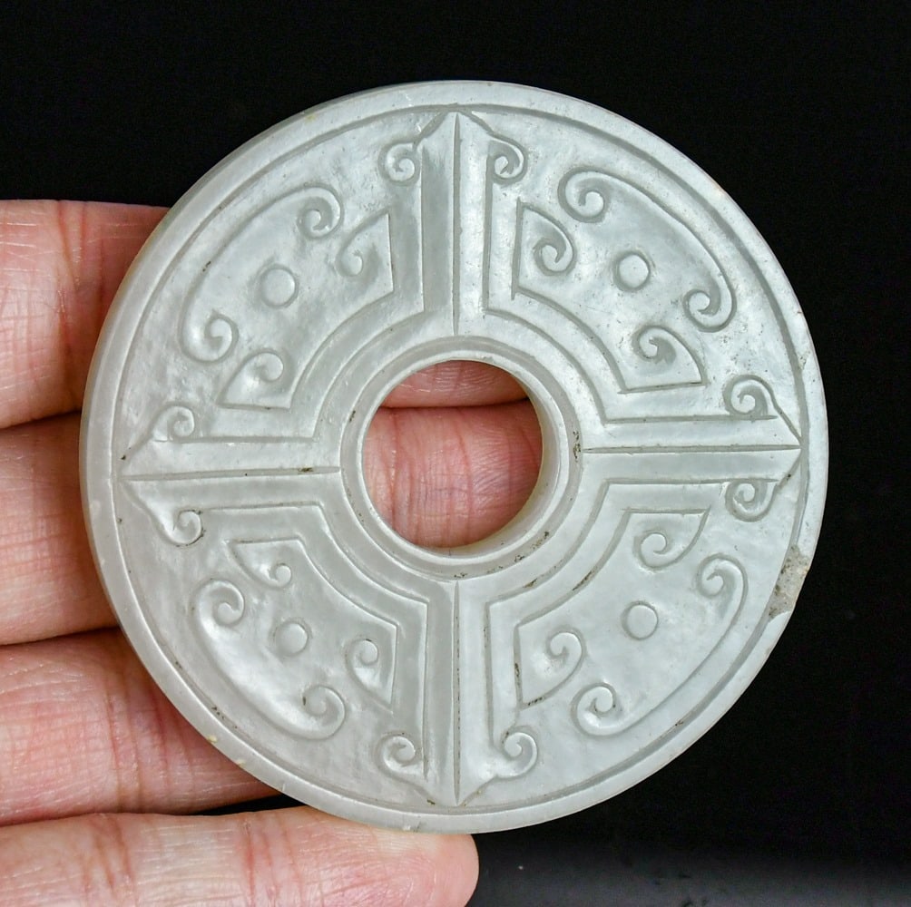 A White Jade Archaic Dragon Bi Disc Qing: The circular disc is carved from a translucent stone of a pale celadon-white tone with minor natural inclusions. Both faces are intricately worked in low relief, divided by incised lines into four sym