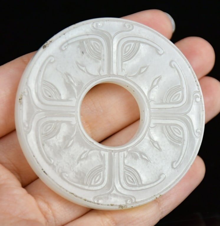 A White Jade Carved Bi Disc Qing: Of characteristic flattened circular form, the body is dynamic and carved in low relief with stylized chilong dragons amid scrolling clouds on one side and grain pattern on the other side. The stone i