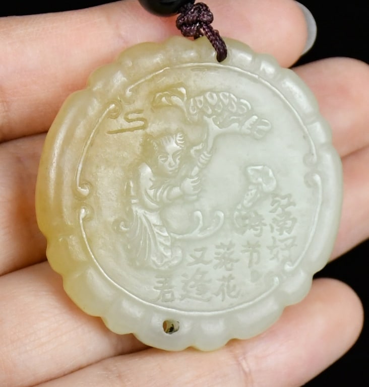 A Celadon Jade Round Pendant Qing: A round jade pendant with one side carved figural story scene while the other side with inscription. The stone in celadon color tone with caramel inclusion part. D:4cm 清 青白玉