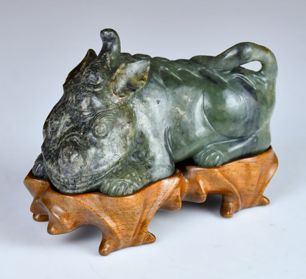 A Lrg Green & Russet Jade Carved Beast Republican: Sculpted in a recumbent position with its muscular limbs tucked close to the body, the mythical creature is depicted with a broad, rounded head turned slightly forward, showcasing bulging. A single