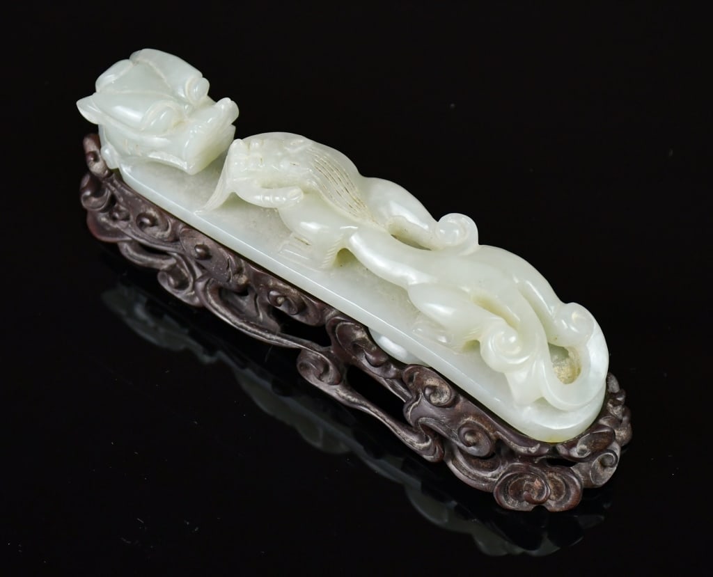 A Carved Jade Dragon Belt Hook w/Std: Carved from a stone of pale celadon showing soft translucency and fine natural inclusions. The curved shaft is sculpted in high relief with a small, sinuous crawling chilong facing the larger, termina