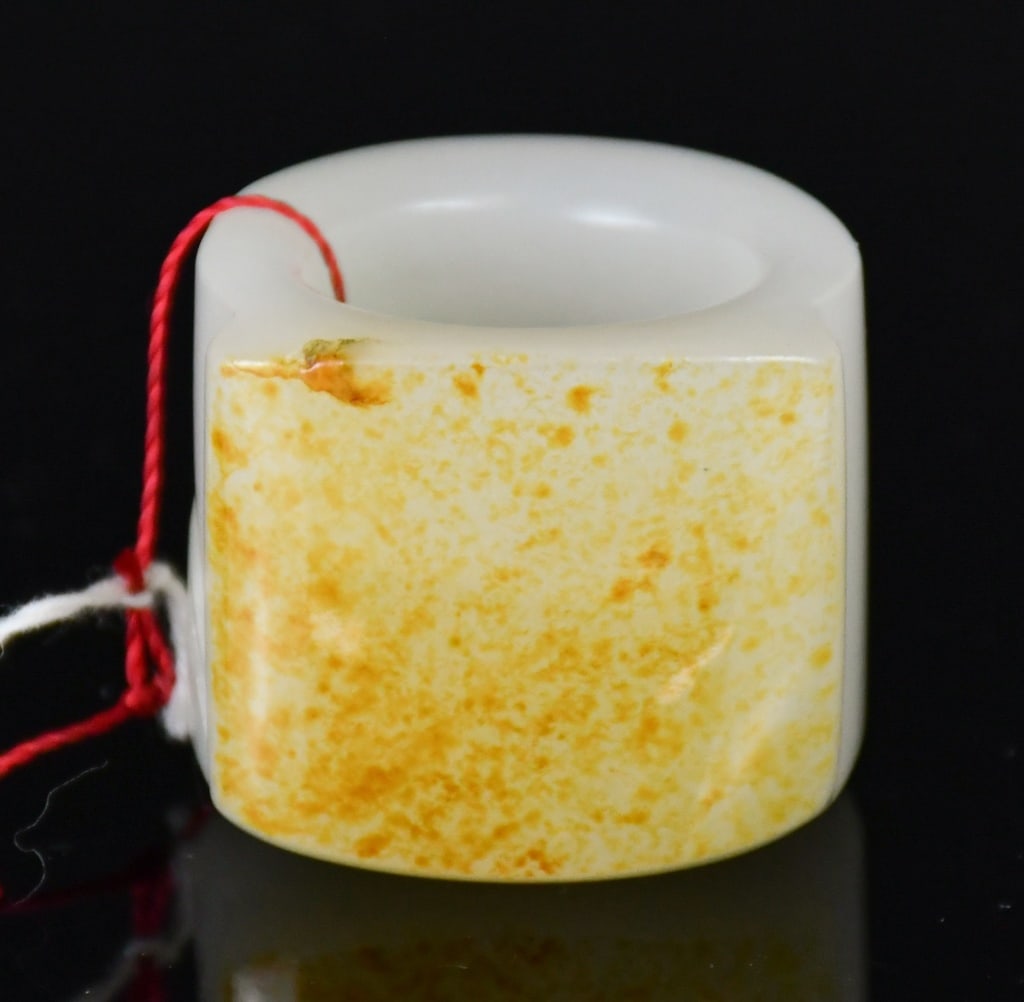 A White Jade Thumb Ring Qing: of cylindrical form, carved with a landscape scene featuring pavilions amidst rockwork, the stone of white tone with russet inclusions. H: 2.7cm, D: 2.1cm 清 白玉雕山