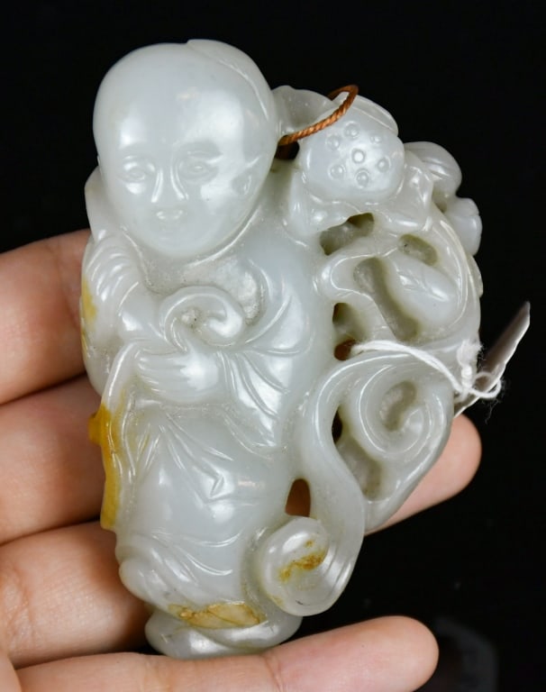 A White Jade Carved Figure Qing: Modelled as a standing child holding a lotus spray, beside scrolling foliage, the stone of pale celadon-white tone with minor russet inclusion. 7.7x5.1cm 清 白玉雕童é